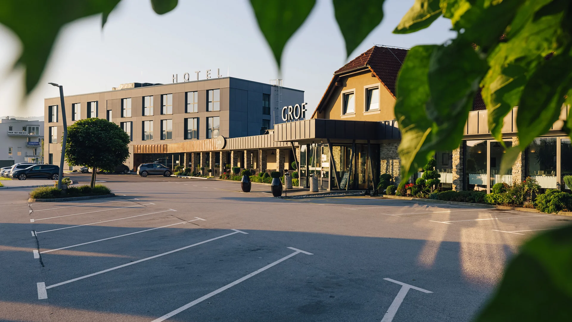 Hotel building with parking lot framed by green leaves in sunset light