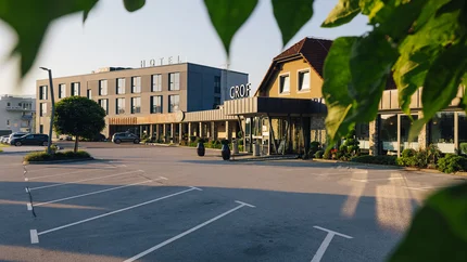 Hotel building with parking lot framed by green leaves in sunset light