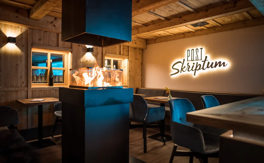 Gemütlicher Holzraum mit modernem Kamin und beleuchtetem Schriftzug Post Skriptum