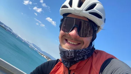 Bikepacking von Wien nach Athen © Jan Koller Mann mit Fahrradhelm und Sonnenbrille lächelt vor Meereskulisse