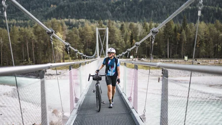 Radfahrer mit Helm schiebt Fahrrad über Hängebrücke in Waldgebiet