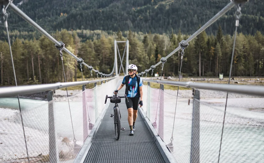 Radfahrer mit Helm schiebt Fahrrad über Hängebrücke in Waldgebiet