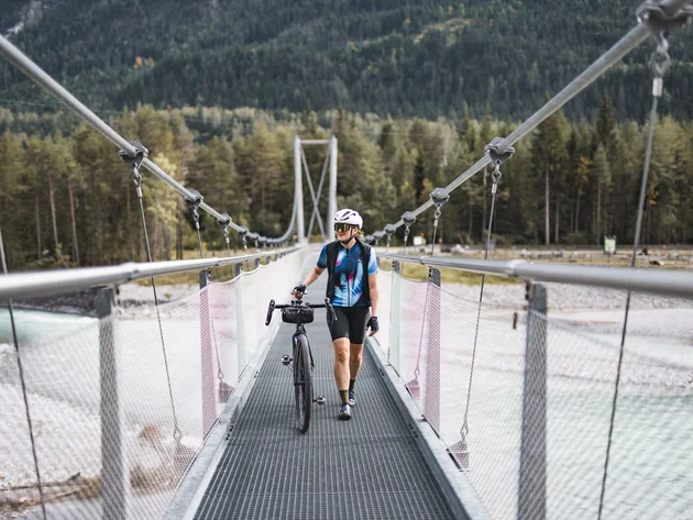 Radfahrer mit Helm schiebt Fahrrad über Hängebrücke in Waldgebiet