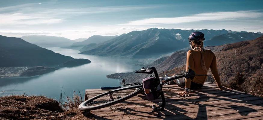 Checklist für das Bikepacking-Abenteuer © Maria Wilke Fahrradfahrerin sitzt auf Holzbühne mit Blick auf See und Berge
