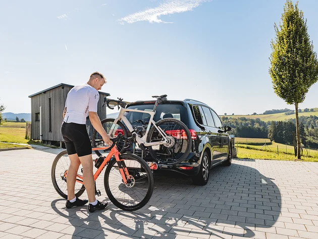 Gravelbiken im Bayerischen Wald © Stefan J. Wolf Photography Mann befestigt Fahrrad an Fahrradträger hinten am Auto auf sonnigem Landparkplatz