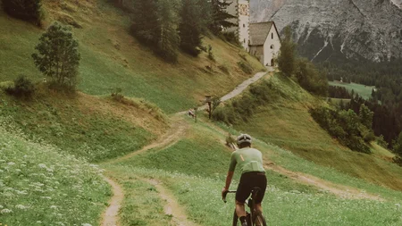 Cyclist riding on a path with church and mountains in the background