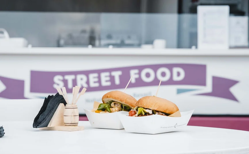 Two street food burgers on a white table with napkin holder