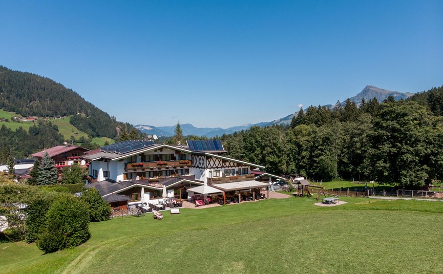 Berghotel mit Solarpanels umgeben von Wiesen und Bergen bei klarem Himmel