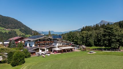 Berghotel mit Solarpanels umgeben von Wiesen und Bergen bei klarem Himmel