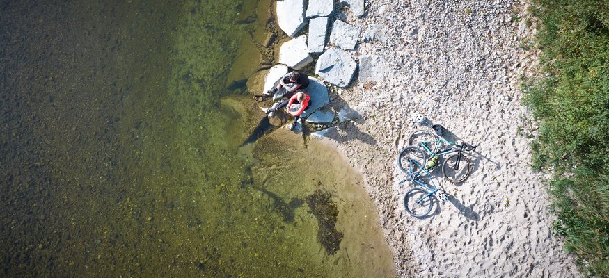 Zwei Radfahrer sitzen am Ufer neben zwei Fahrrädern