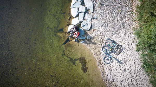 Deutschland © Oberbayern.de - Tobias Köhler Zwei Radfahrer sitzen am Ufer neben zwei Fahrrädern