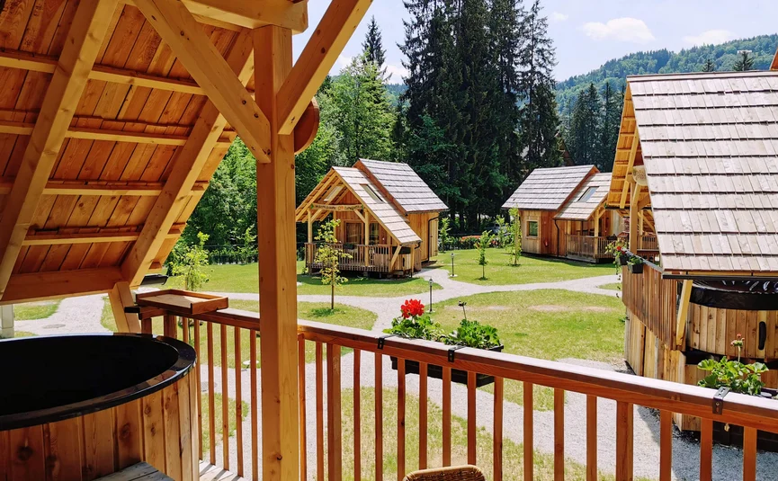 View from balcony with wooden tub to wooden cabins and garden in forest