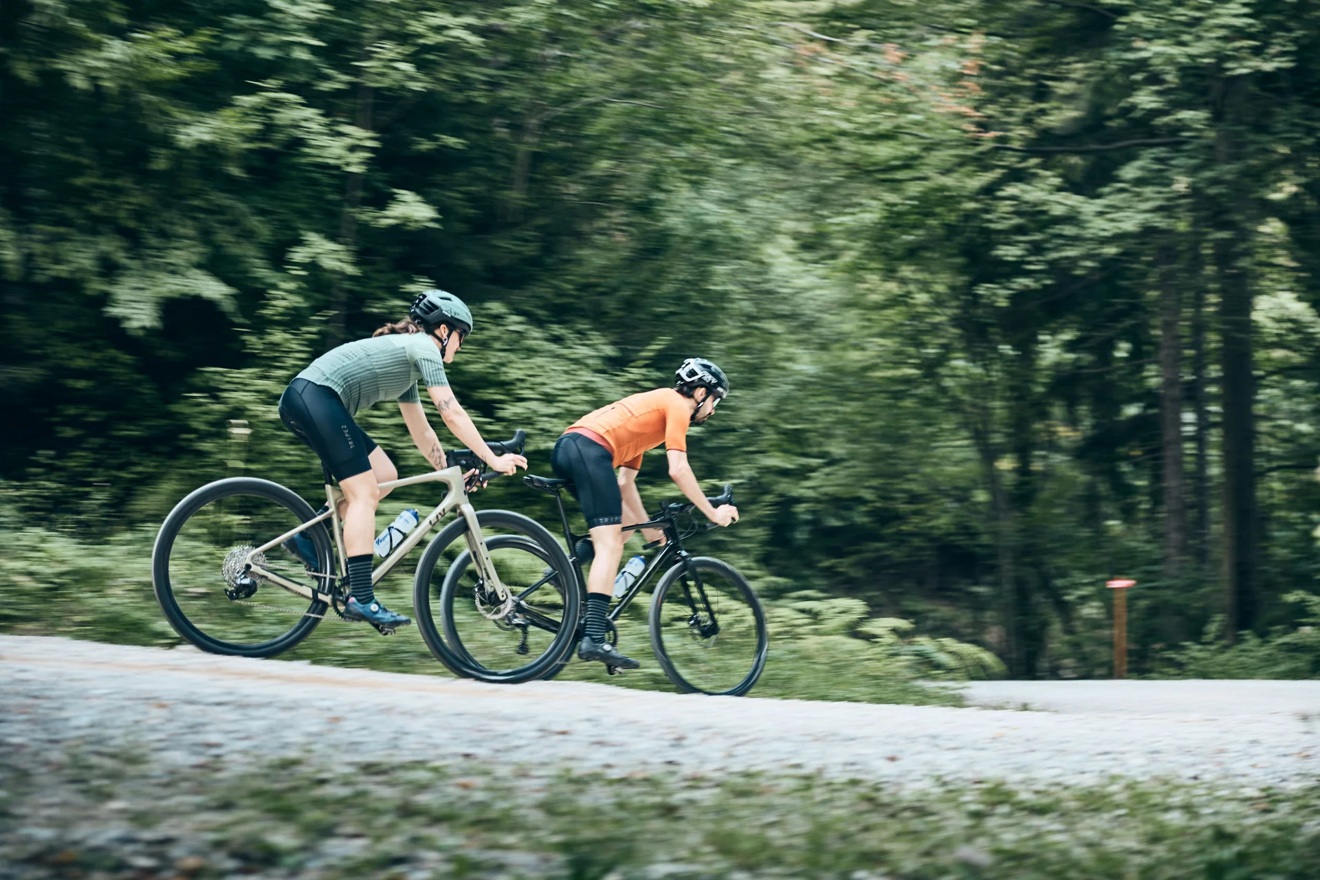 Gravelbike Holidays © Tobias Köhler Zwei Radfahrer fahren auf einem Waldweg mit grünem Hintergrund