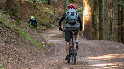 Mountainbiker fahren auf Waldweg mit Helm und Rucksack
