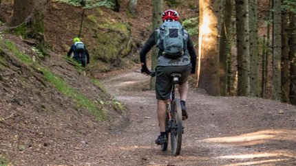 Mountainbiker fahren auf Waldweg mit Helm und Rucksack