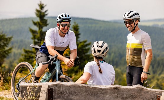 Three cyclists chatting on a forest trail with bikes and helmets