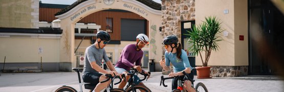 Drei Radfahrer in Sportkleidung beraten sich vor historischen Gebäuden