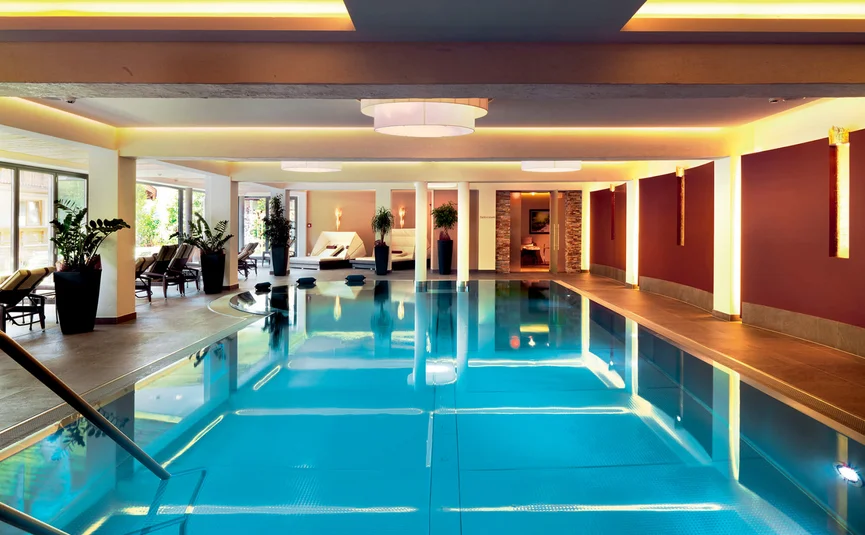 Aktivhotel Alpendorf **** © Atelier Oczlon Innenbereich eines modernen Schwimmbads mit Liegestühlen und Pflanzen