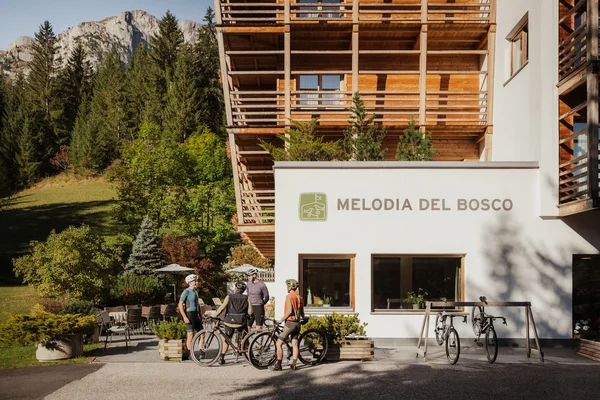 Alpine Gravel Experience © Alex Moling Cyclists standing outside Melodia del Bosco hotel in a mountain setting