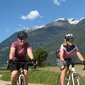 Two women cycling on a trail with mountains in the background