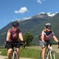 Zwei Frauen radeln auf einem Weg mit Bergen im Hintergrund