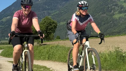 Two women cycling on a trail with mountains in the background