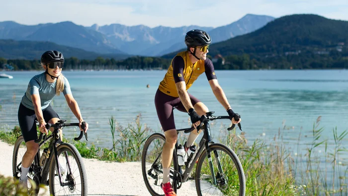 Zwei Radfahrer fahren auf einem Weg entlang eines Sees bei sonnigem Wetter