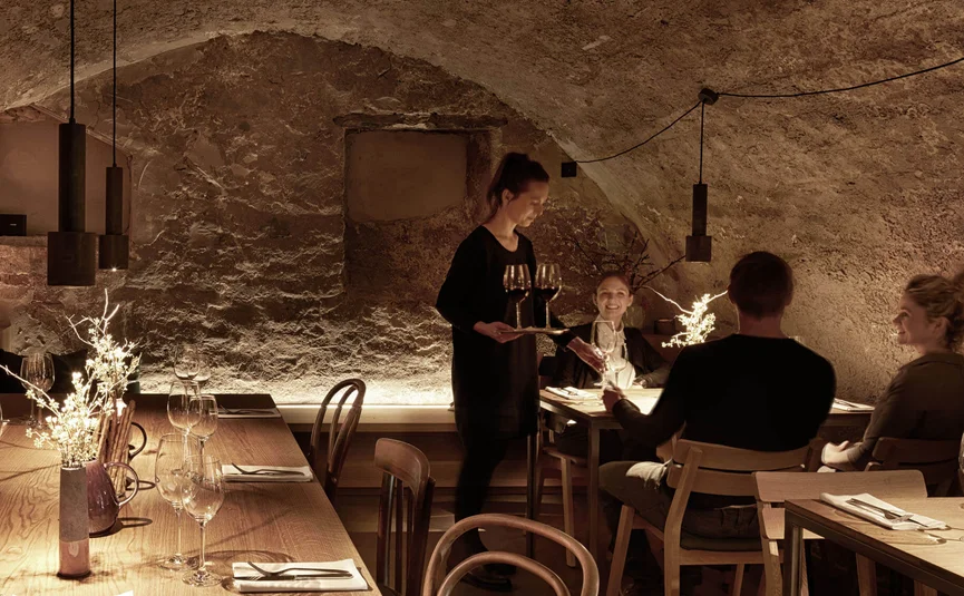 Kellnerin serviert Wein an Gäste in einem gemütlichen Restaurant mit Steinmauer