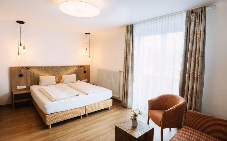 Helles Hotelzimmer mit Doppelbett, Sesseln und großem Fenster mit Vorhängen