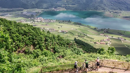 Gravel & Törggelen: Warum Tramin im Herbst perfekt für Gravelbiker ist © Heiko Mandl Drei Radfahrer schauen von Aussichtspunkt auf See und grüne Täler