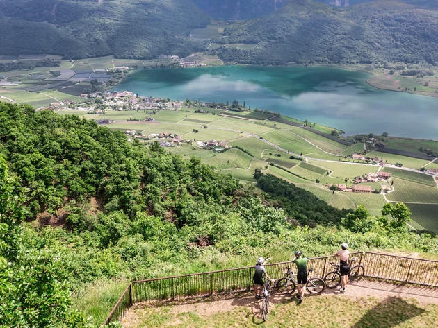Gravel & Törggelen: Warum Tramin im Herbst perfekt für Gravelbiker ist © Heiko Mandl Drei Radfahrer schauen von Aussichtspunkt auf See und grüne Täler