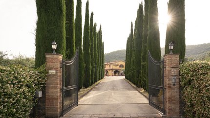 Eingangstor zu einem Anwesen mit Zypressenallee und Haus im Hintergrund