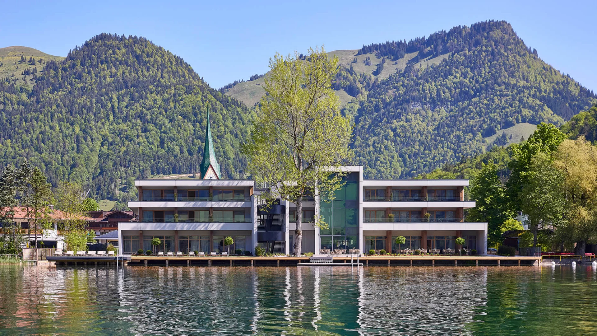 Epic Route Vorarlberg - Salzburg © Simon Hausberger Modern building by lake with forested mountains and clear sky