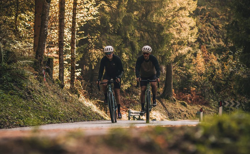 Two cyclists on a hilly forest road in autumn
