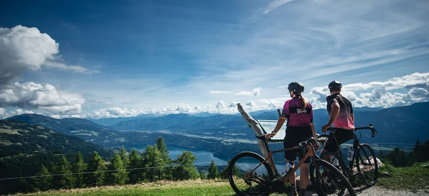 Zwei Radfahrer schauen auf Bergsee und Berge an einem klaren, sonnigen Tag.