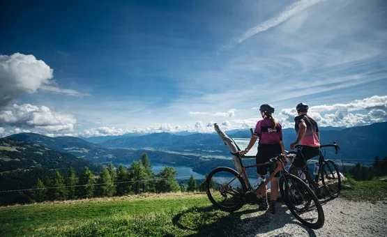 Gravelbike Urlaub in der NOCKBIKE Area © Nicola Littmann Zwei Radfahrer schauen auf Bergsee und Berge an einem klaren, sonnigen Tag.