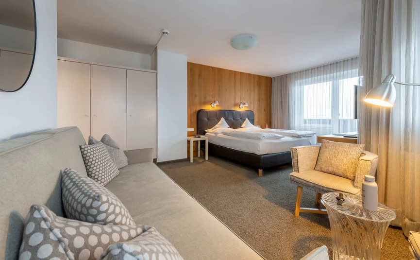 Modern hotel room with bed, sofa, armchair, and sheer curtains