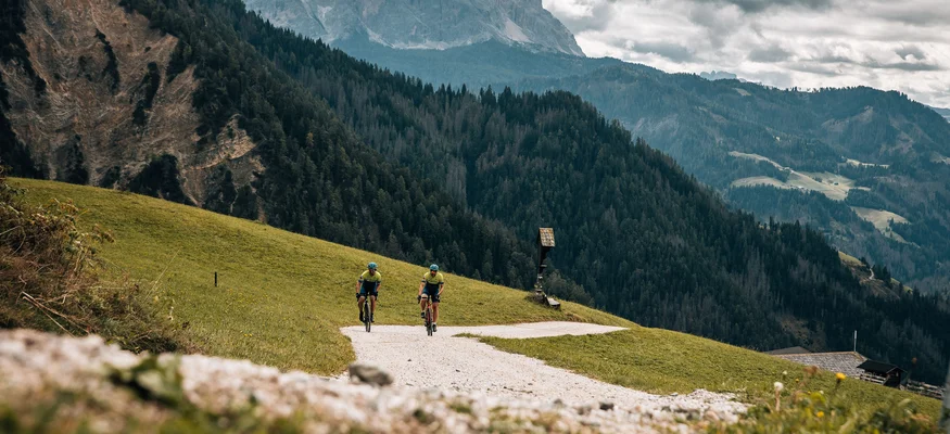 Zwei Fahrräder fahren auf einem Bergweg mit bewaldeten Bergen im Hintergrund