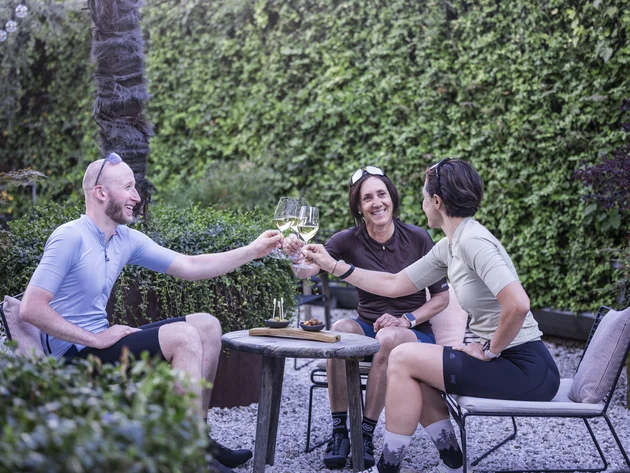 Gravel & Törggelen: Warum Tramin im Herbst perfekt für Gravelbiker ist © Heiko Mandl Drei Radfahrer stoßen beim Entspannen im Garten mit Wein an