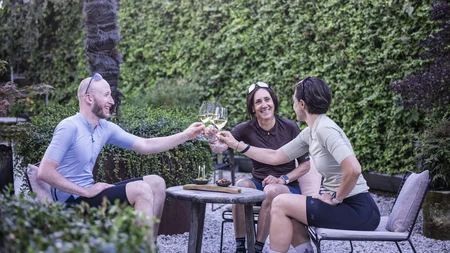 Gravel & Törggelen: Warum Tramin im Herbst perfekt für Gravelbiker ist © Heiko Mandl Drei Radfahrer stoßen beim Entspannen im Garten mit Wein an