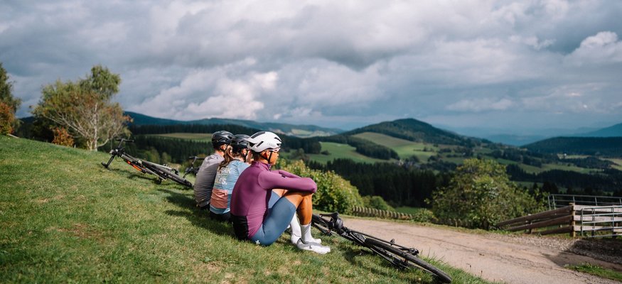 Drei Radfahrer sitzen auf einer Wiese und betrachten die Berglandschaft