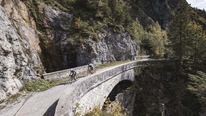 Zwei Radfahrer auf einer Steinbrücke in bergiger Landschaft