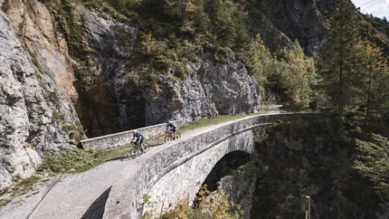 Two cyclists on a stone bridge in a mountainous landscape