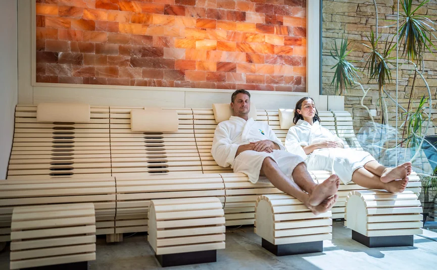 Entspannendes Paar in Bademänteln auf Holzliegen in einer Spa-Sauna