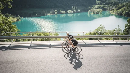 Two cyclists riding by a lake in a mountainous landscape