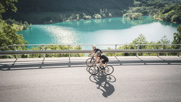 Zwei Radfahrer fahren an einem See in bergiger Landschaft vorbei