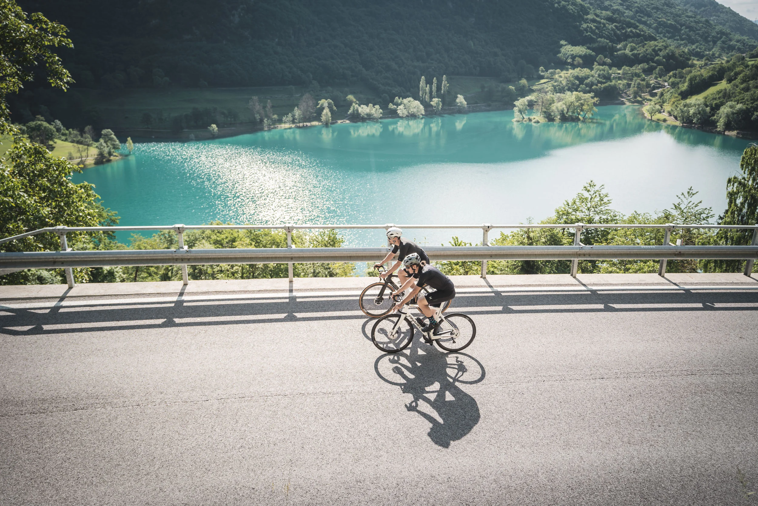 Epic Route Dolomites – 3 Zinnen – Gardasee © APT Garda Dolomiti Zwei Radfahrer fahren an einem See in bergiger Landschaft vorbei
