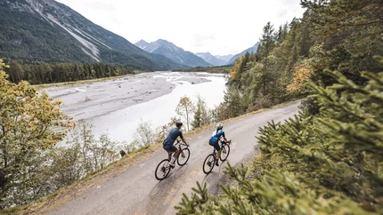 Zwei Radfahrer fahren auf einem Waldweg am Flussufer in den Bergen