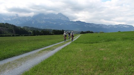 Rund um die Hohe Salve © Michael Küchl Drei Radfahrer auf einem Feldweg mit Bergen und bewölktem Himmel im Hintergrund