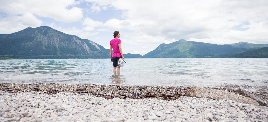 Frau steht im See und blickt auf Berge unter bewölktem Himmel